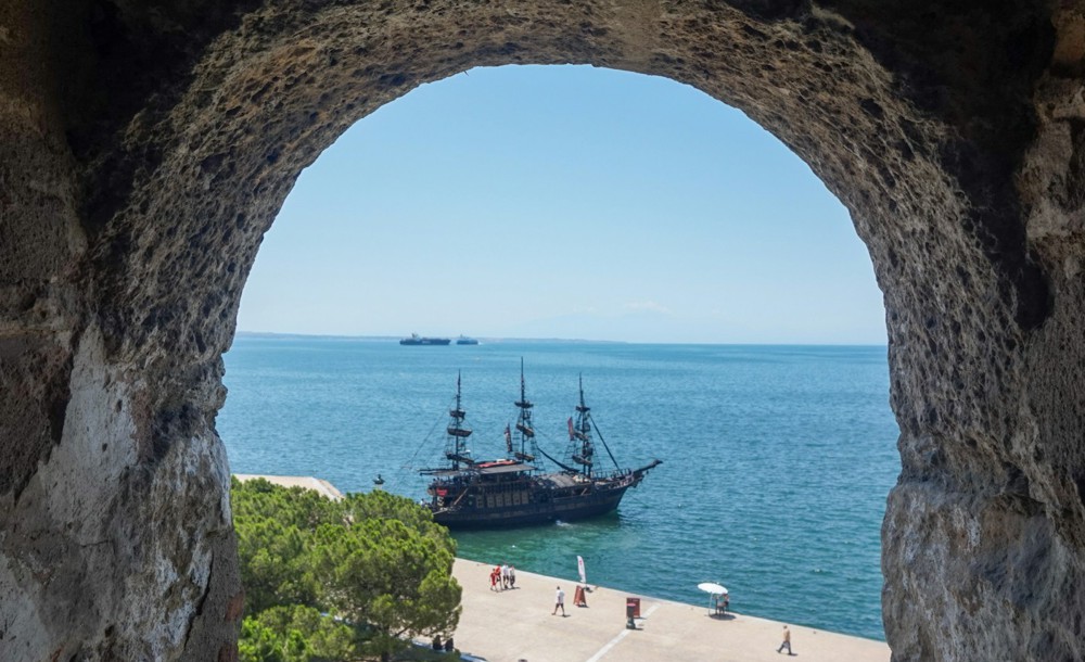 Θέα προς τον Θερμαϊκό κόλπο μέσα από πέτρινη καμάρα, με πειρατικό πλοίο και καθαρό γαλάζιο ουρανό.