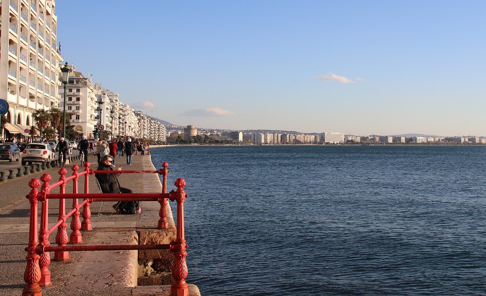 Παραλία Θεσσαλονίκης με θέα στον Θερμαϊκό κόλπο και τον Λευκό Πύργο στο βάθος, κάτω από καθαρό γαλανό ουρανό.
